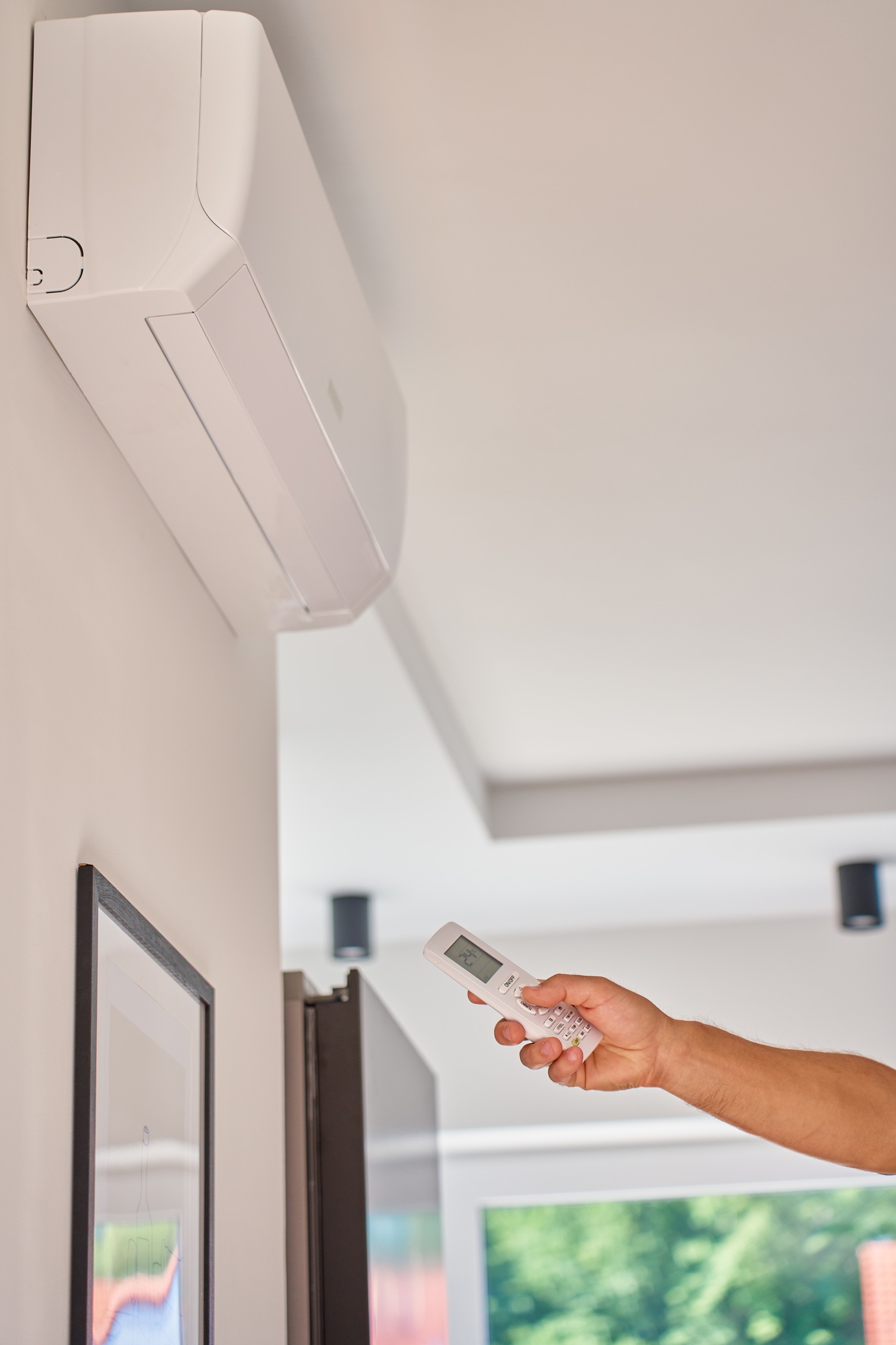 Hand using remote control to adjust temperature on air conditioner at home